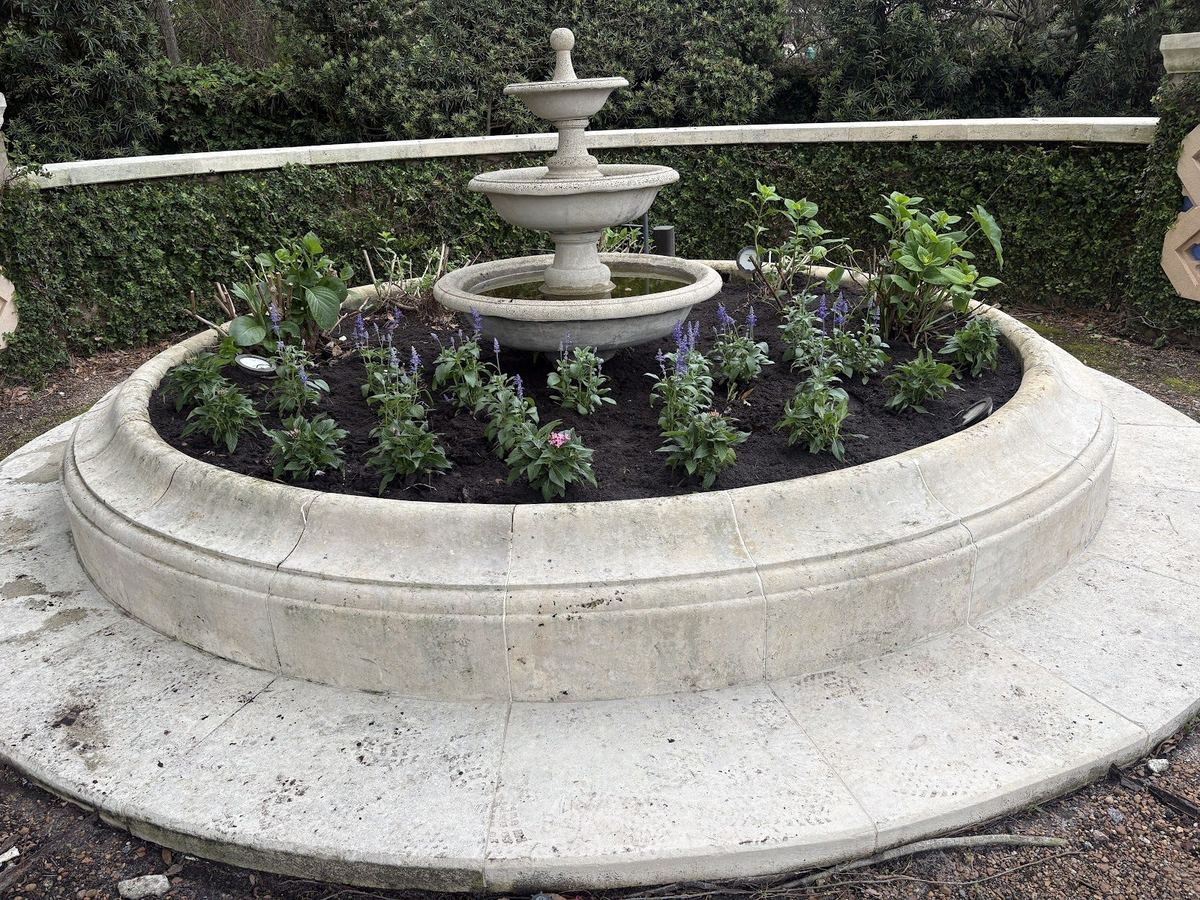 Circular planting bed with new plants around a stone fountain, installed by Prestige Landscaping