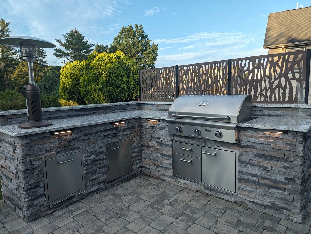 An inviting outdoor kitchen with stone countertops and a built-in grill under a pergola.